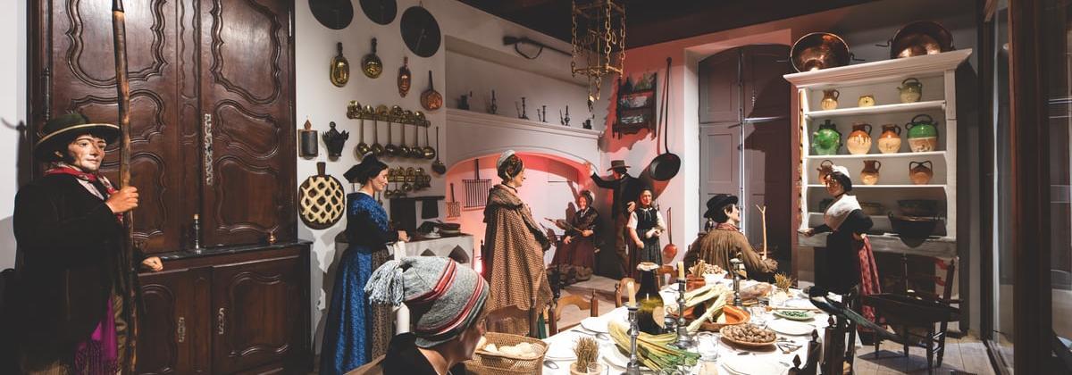 gros plan sur une reconstitution d'une salle à manger provençale avec des casseroles aux murs des placards et une grande tablée couverte de mets provençaux