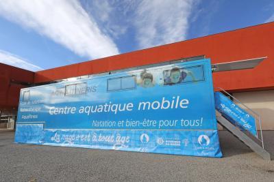 Camion bleu Centre Aquatique Mobile garé devant un bâtiment rouge. Il s'agit d'un camion piscine du Département des Bouches-du-Rhône - Agrandir l'image 1 sur 4, fenêtre modale