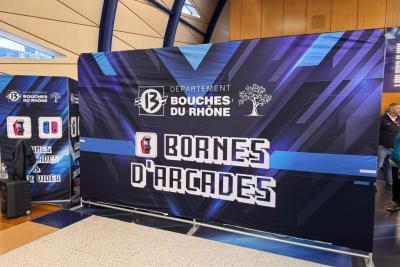 Lors du Mercredi sport et e-sport des Bouches-duRhône, un stand aux couleurs bleu, noir et blanc présente des bornes d’arcade. Le décor affiche “Département Bouches du Rhône” et “Jeux Vidéo” dans un style moderne et numérique. Des machines de jeux rétro sont visibles à gauche, prêtes à accueillir les visiteurs dans une ambiance ludique et technologique. - Agrandir l'image 4 sur 5, fenêtre modale