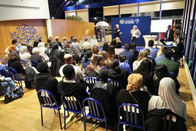 Vue d’ensemble d’une salle avec un public assis sur des chaises bleues, face à une scène où deux intervenants s’expriment devant un panneau « Département Bouches-du-Rhône ». - Agrandir l'image 1 sur 3, fenêtre modale