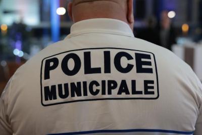 Un adulte vu de dos porte un polo blanc avec l’inscription “POLICE MUNICIPALE” en grands caractères bleu marine. Il se trouve dans un espace intérieur éclairé, avec d’autres personnes en uniforme autour, suggérant un rassemblement institutionnel. Il s'agissait de la cérémonie des voeux au personnel des forces de l'ordre et de secours des Bouches-du-Rhône. - Agrandir l'image 6 sur 18, fenêtre modale