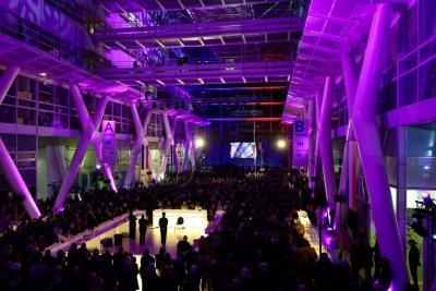 Vue d’ensemble d’un vaste hall éclairé en violet, rempli de participants lors d’un événement avec scène au fond - Agrandir l'image 6 sur 20, fenêtre modale