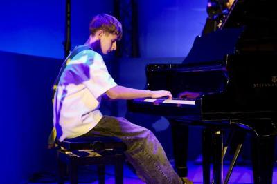 Jeune musicien jouant du piano à queue sur une scène éclairée en bleu durant un événement - Agrandir l'image 16 sur 20, fenêtre modale