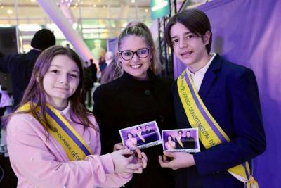 Trois jeunes portant des écharpes officielles et tenant des photos souvenirs lors d’un événement dans un hall lumineux - Agrandir l'image 7 sur 20, fenêtre modale