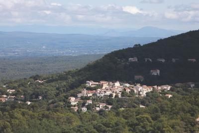 Un petit village est niché sur le flanc d’une colline boisée. À l’arrière-plan, on aperçoit une succession de collines et de montagnes sous un ciel partiellement couvert. - Agrandir l'image 4 sur 4, fenêtre modale