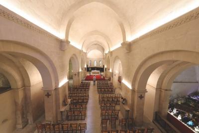 Intérieur d’une église ou chapelle avec de hauts plafonds voûtés. Des rangées de chaises en bois sont orientées vers un autel situé au fond. L’éclairage met en valeur les détails architecturaux, créant une ambiance calme et solennelle. - Agrandir l'image 4 sur 6, fenêtre modale