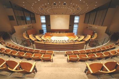 Grande salle de séance publique aménagée par Andrée Putman, avec des rangées de sièges en bois autour d'un espace central éclairé. La salle est très éclairée. - Agrandir l'image 1 sur 3, fenêtre modale