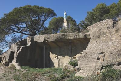 Statue blanche sur un piédestal, entourée d’arbres, dominant des roches taillées avec cavités et piliers métalliques, sous un ciel bleu. - Agrandir l'image 5 sur 6, fenêtre modale